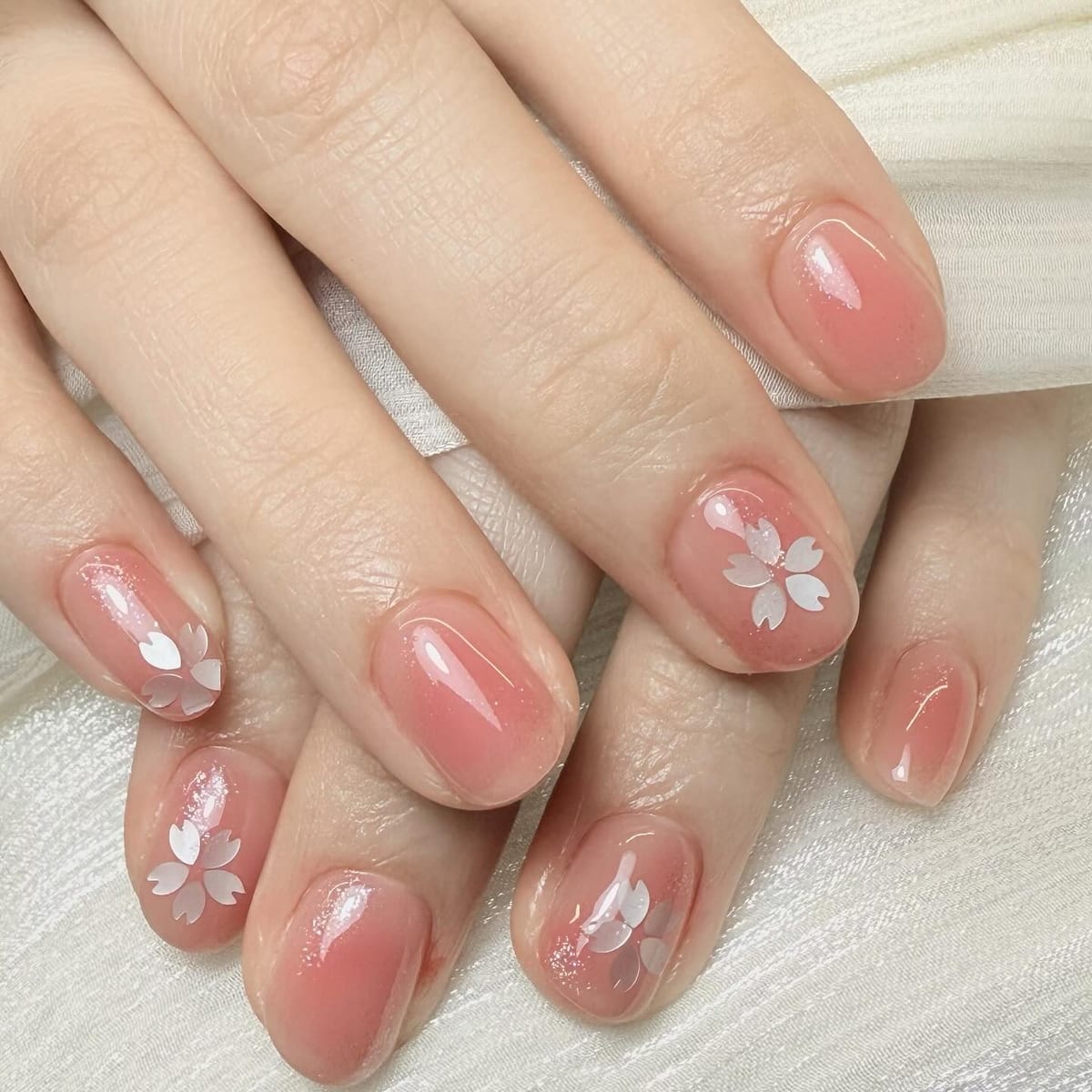 珊瑚果冻透亮指甲缀细腻珠光,点缀白色樱花花瓣造型,浪漫唯美