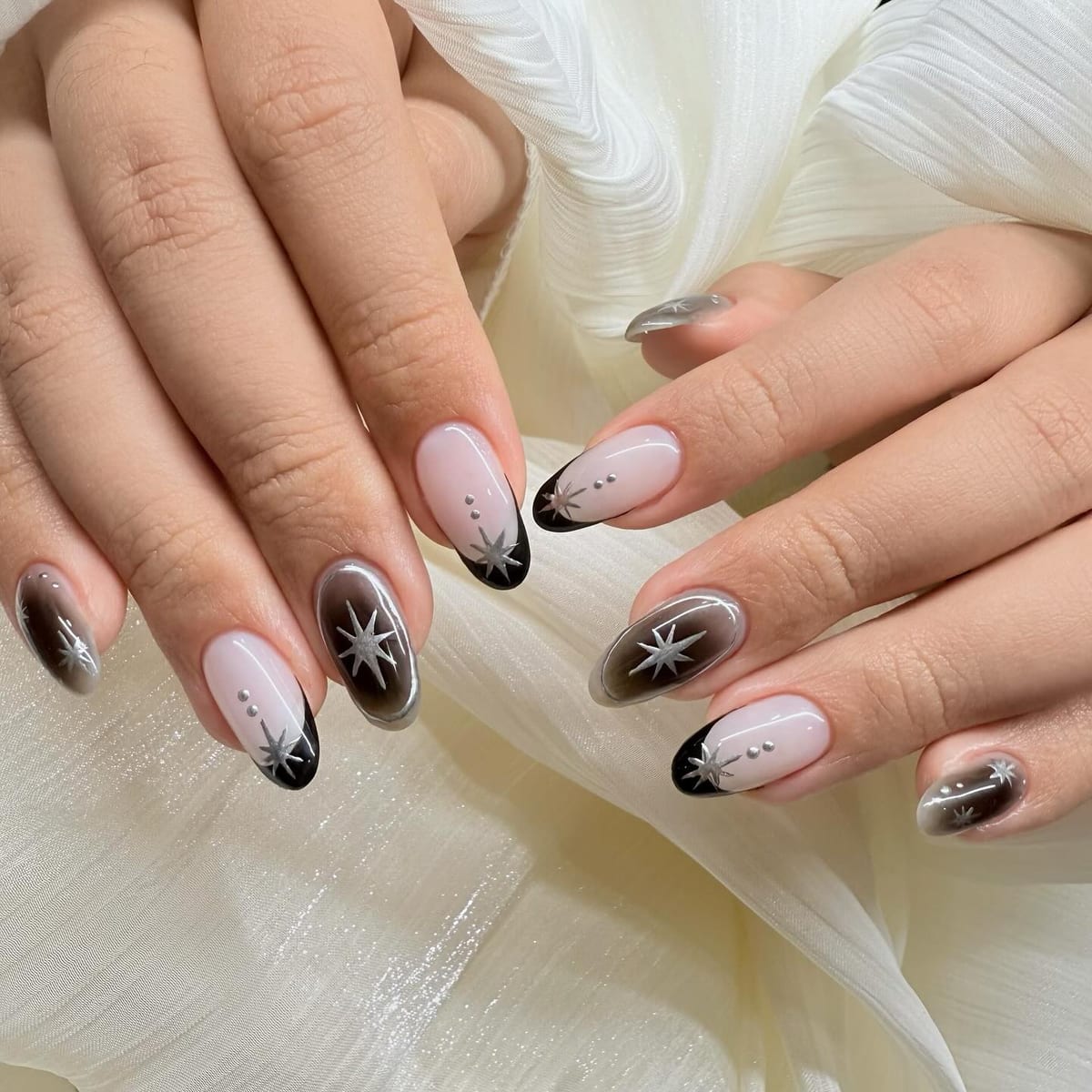Almond nails in nude with sleek black cat-eye French tips and silver starburst line art